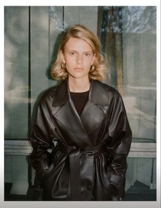 a woman standing in front of a window wearing a black leather coat