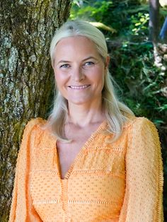 a woman standing in front of a tree wearing an orange dress and smiling at the camera