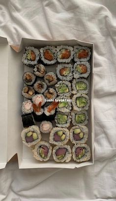 an open box filled with sushi on top of a white sheet covered tablecloth