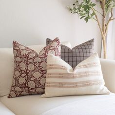 three pillows on a white couch in front of a potted plant