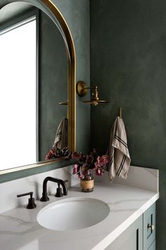 a bathroom with green walls and white counter tops, gold faucet mirror above the sink