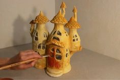 a person is painting a clay house with paintbrushes on a table in front of a white wall