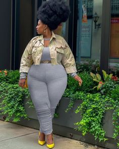 a woman with an afro is walking down the street wearing grey pants and yellow heels