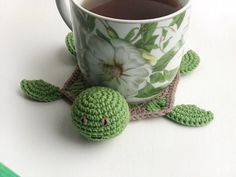 a crocheted turtle sits next to a cup of tea