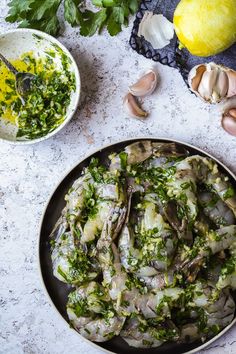 a pan filled with food next to lemons and parsley on a white table