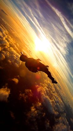 a person is flying through the air with clouds and sun in the backgroud