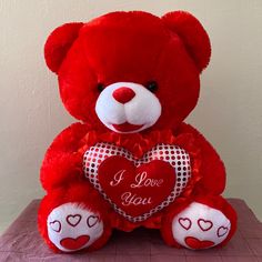 a red teddy bear sitting on top of a table with a heart in the middle