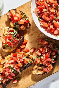 grilled bread topped with tomatoes and herbs next to a bowl of dressing on a cutting board