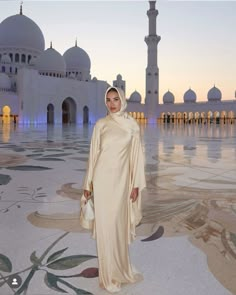 a woman standing in front of a white building at sunset with her hands on her hips