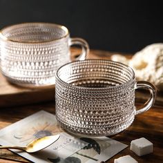 two glass mugs sitting next to each other on top of a wooden table with sugar cube