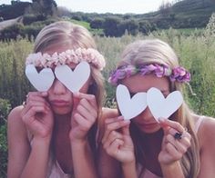 two young women holding up paper hearts in front of their faces with flowers on them