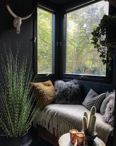 a living room filled with lots of furniture next to a window covered in plants and pillows