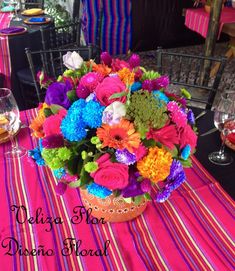 colorful flowers are arranged in a basket on a striped tablecloth with wine glasses and plates