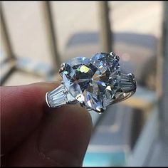 someone is holding an engagement ring with a large diamond in the center and two baguetts on each side