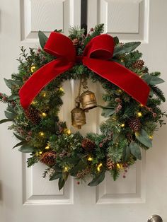 a christmas wreath with a bell and red bow hanging on the front door to welcome guests