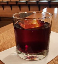 a glass filled with liquid sitting on top of a wooden table next to a white napkin