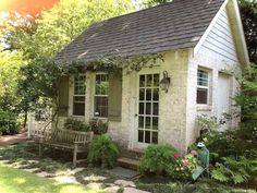 a small white house sitting in the middle of a lush green yard with lots of trees