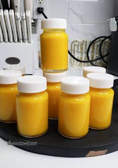 six jars of yellow liquid sitting on top of a counter