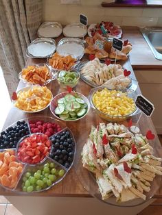 an assortment of food is displayed on a table in front of the kitchen window, along with other snacks and condiments