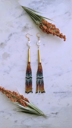 three pairs of earrings on top of a marble counter with dried flowers and leaves in the foreground