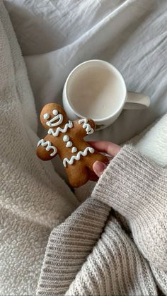 a person holding two ginger cookies next to a cup of coffee on top of a bed