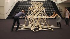 three people standing around a wooden structure on the floor in front of some bleachers