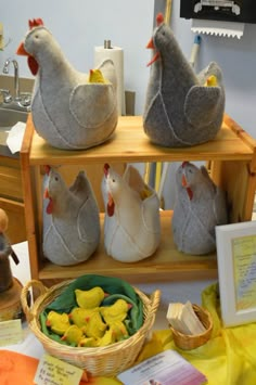 three stuffed chickens sitting on top of a wooden shelf next to a basket filled with chicks