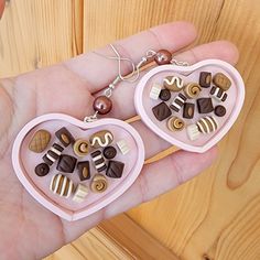 a pair of heart shaped earrings with chocolates and candy on them are being held by a person