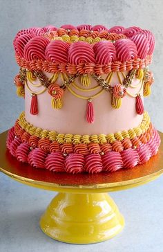 a pink and yellow cake with tassels is on a gold plated stand