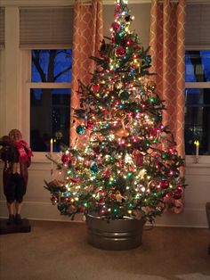 a decorated christmas tree in a living room next to a window with red and green lights