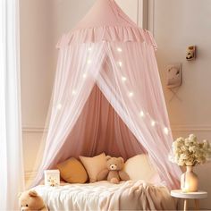 a pink canopy bed with white lights and teddy bears on the pillows in front of it