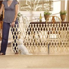 a woman standing next to a white dog near a table with chairs and a vase on it