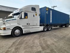 a white semi truck parked in front of a building with a blue trailer behind it