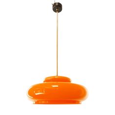 an orange pendant light hanging from a metal rod on a white wall with a small black object in the background