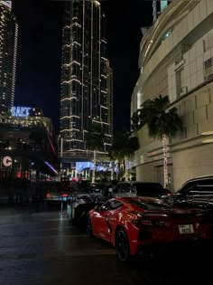 several cars parked on the side of a street at night with tall buildings in the background