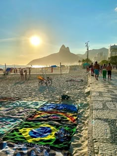 people walking on the beach at sunset with blankets and towels laid out in front of them