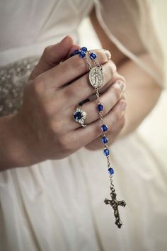 a woman in a white dress is holding a rosary and wearing a blue beaded bracelet