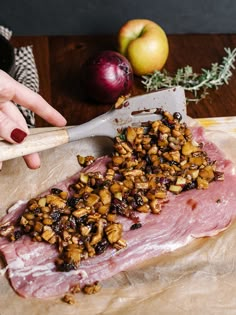 a person is cutting meat with nuts on it and an apple in the background next to them