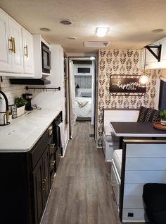 a narrow kitchen with white cabinets and wood flooring is seen in this image from the hallway