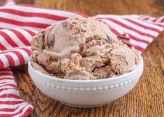 a bowl filled with ice cream sitting on top of a wooden table next to a red and white striped napkin