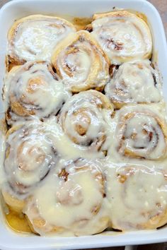 a white dish filled with cinnamon rolls covered in icing