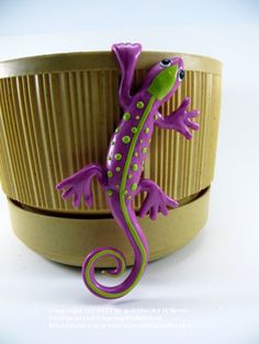 a purple and green toy gecko sitting on top of a wooden bowl in front of a white background