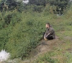 a man sitting on the side of a hill next to a lush green forest filled with trees