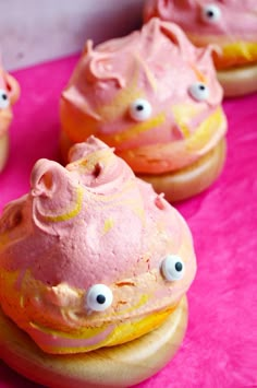 pink frosted doughnuts with googly eyes on them sitting on a pink surface