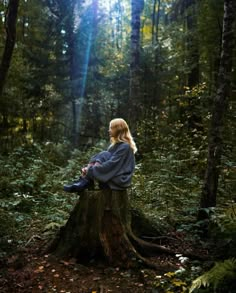 a woman sitting on top of a tree stump in the woods