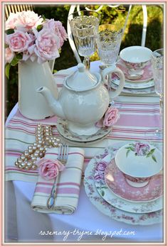 a pink and white table setting with teapot, plates, napkins and flowers