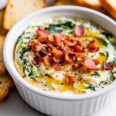 a bowl of dip with bacon and spinach in it next to some crackers