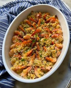 a white bowl filled with shrimp and rice on top of a blue striped towel next to a spoon