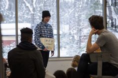 a man standing in front of a group of people sitting down and talking to each other