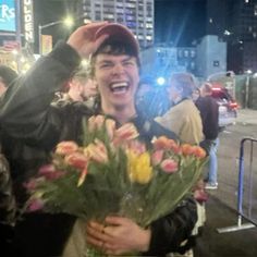 a man is holding flowers and smiling at the camera while standing in front of a crowd